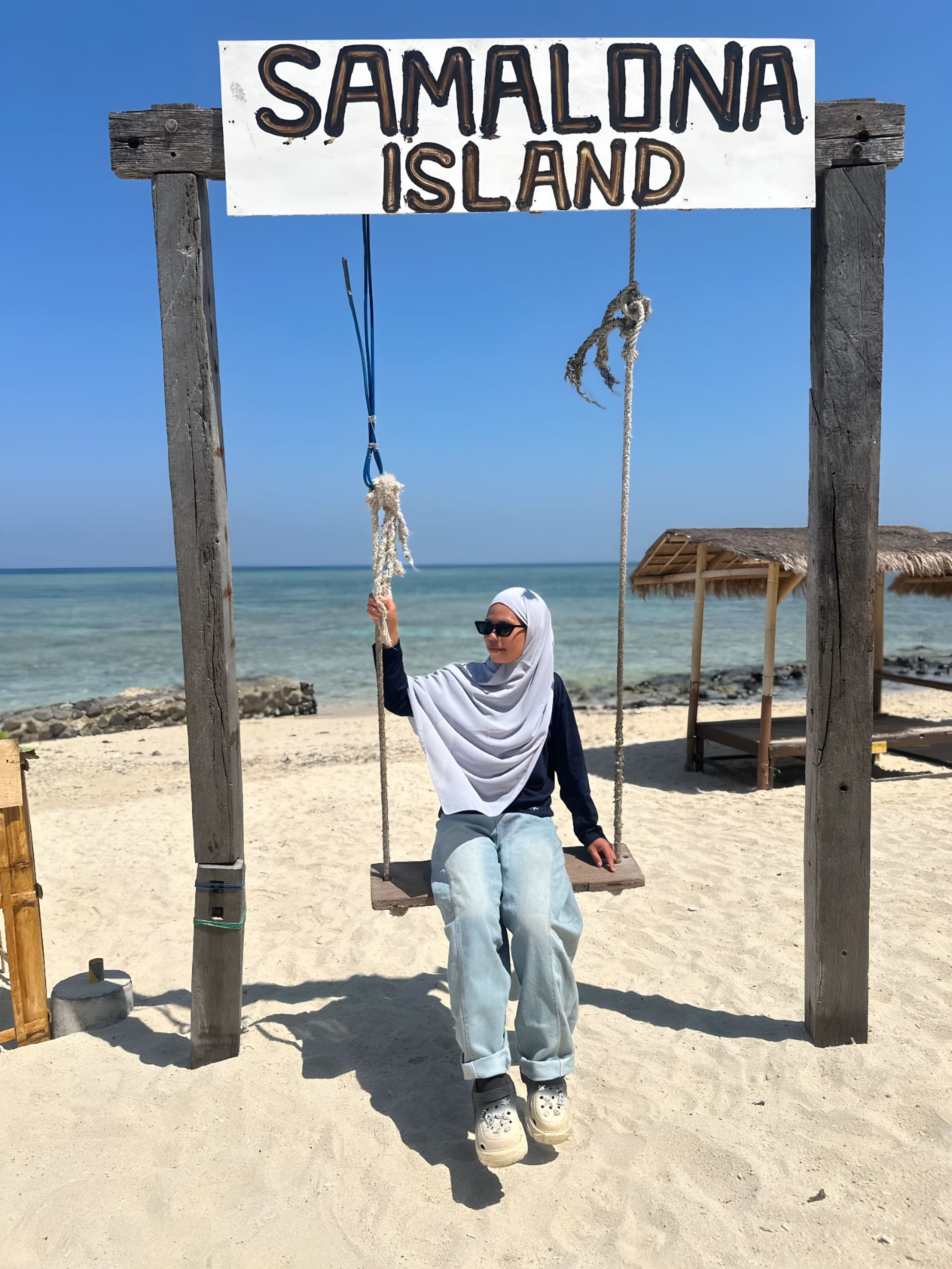 Tamu duduk di ayunan bertuliskan Samalona Island di pantai pasir putih
